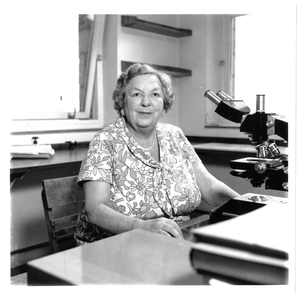 Mary Parke posing with a microscope in her laboratory